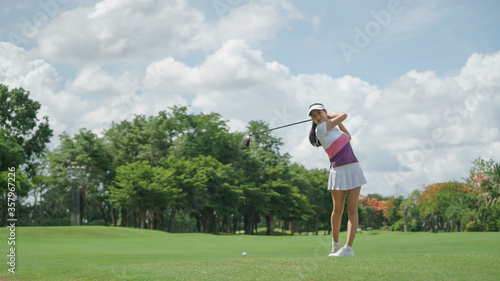 Asian female golfer swinging club on golf course green with copy space. 