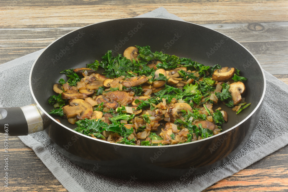 Mushrooms, kale and shallot filling or ingredient sauteed in olive oil in non-stick frying pan on hot towel on table