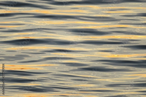 Water surface with yellow sun glare on the waves, natural background