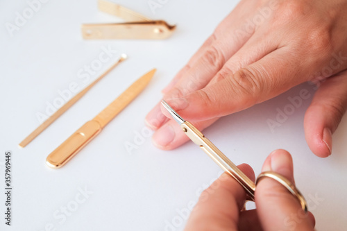 Woman hands using a small scissors to cut her fingernails on a white background. View from above. Manicure at home