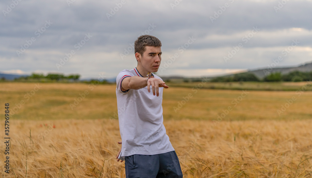 Happy young man pointing to you to join his happiness with outstretched arms standing in a wheat field Happy young man pointing to you to join his happiness with outstretched arms standing in a wheat field