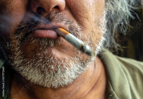 Unshaven bearded man with a cigarette in his mouth close-up.
