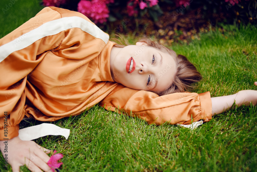 A girl with healthy beautiful hair lies on the grass and looks at the camera. Girl with perfect skin and natural care. Flower in the hands. Layered with eyes closed, sleeping
