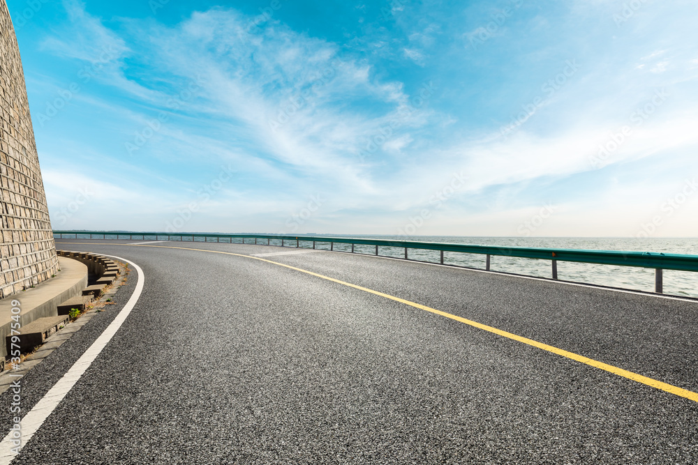 Empty asphalt road and lake under blue sky. Empty asphalt road and lake under blue sky.
