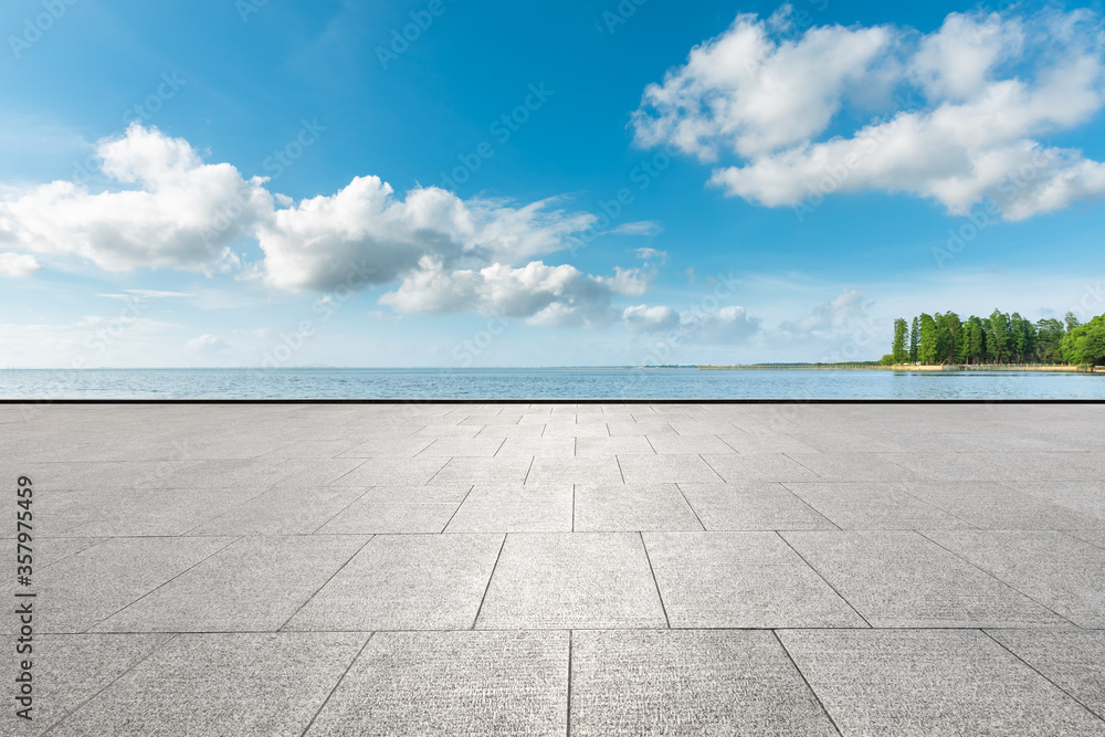 Empty square floor and lake with tree under blue sky.