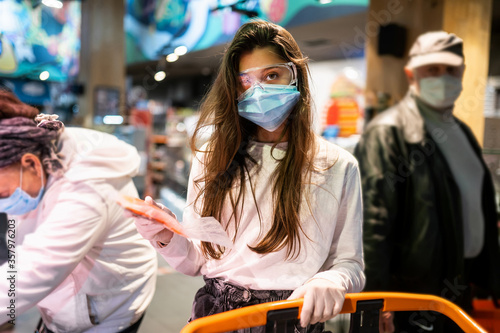 Woman with the surgical mask and the gloves is shopping in the supermarket