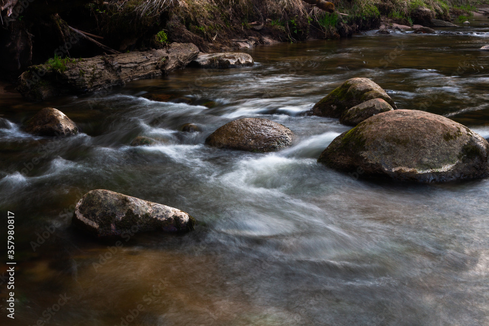 small river in forest with stones at sunset