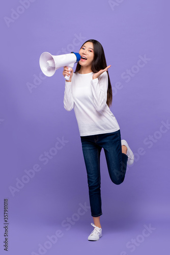 Full body of beautiful Asian woman announcing on magaphone isolated on purple background