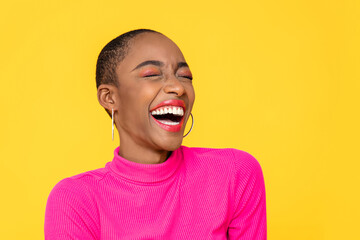Happy optimistic African American woman in colorful pink clothes laughing isolated on yellow background