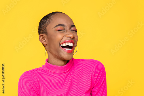 Happy optimistic African American woman in colorful pink clothes laughing isolated on yellow background