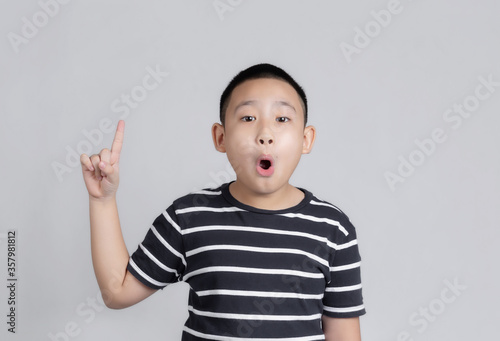 Asian boys studio portrait on gray background with amazed and surprised looking and pointing with fingers and raised arms.
