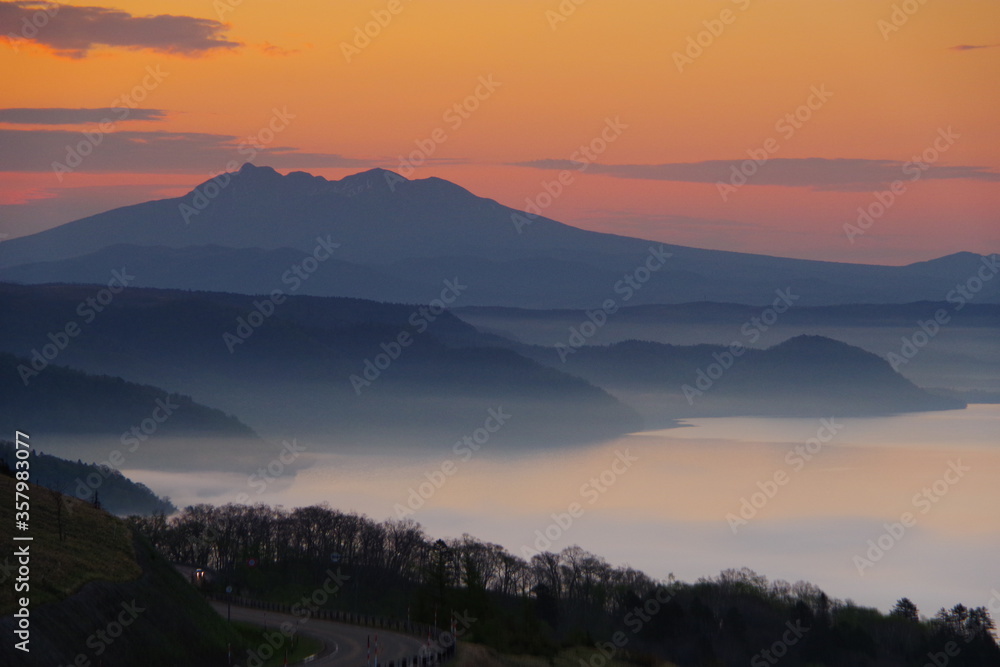 遠くの山のシルエットと朝靄の湖。峠からの風景。美幌峠、北海道、日本。
