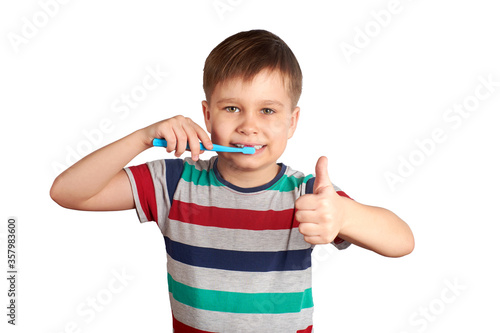Smiling boy brushes his teeth and shows a thumbs up, isolated on a white background