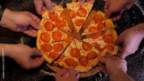 Hands are taking slices of pepperoni pizza away from the wooden board. Black table background.
