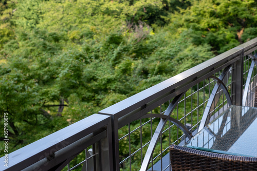 View of restaurant glass table and chair next to terrace railing with a landscape garden of trees in the background