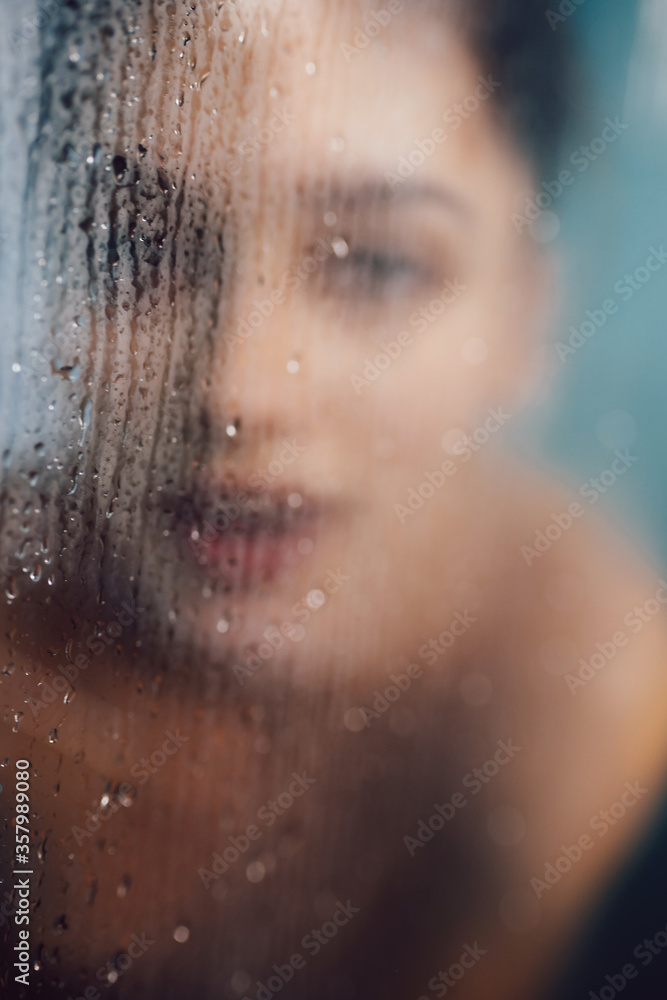 Beautiful woman behind the glass with water drops.