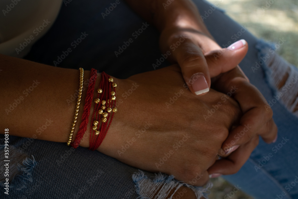 woman's hand with red and gold bracelet on jean pants