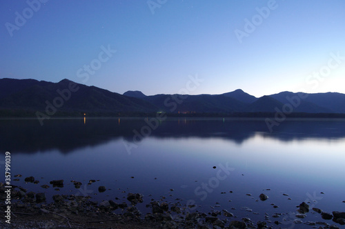 黄昏時の青い湖の風景。水面に映る空の色、遠くの山々のシルエット。