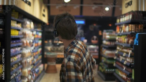 Wallpaper Mural At the Supermarket: Stylish caucasian guy with headphones walks through goods section of the store, wearing plaid shirt. Following back view shot. Slow Motion. Blurred background Torontodigital.ca