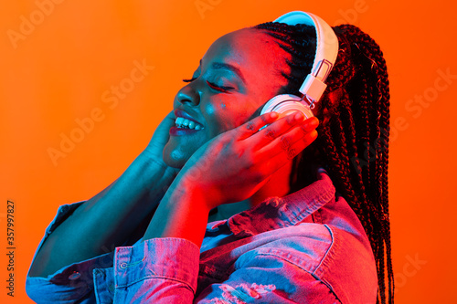 African american young woman listening to music online dancing and singing with headphones, neon light. Music and technology concept.