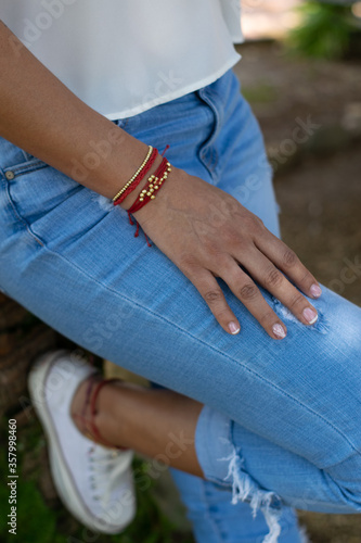woman's hand with red and gold bracelet on jean pants