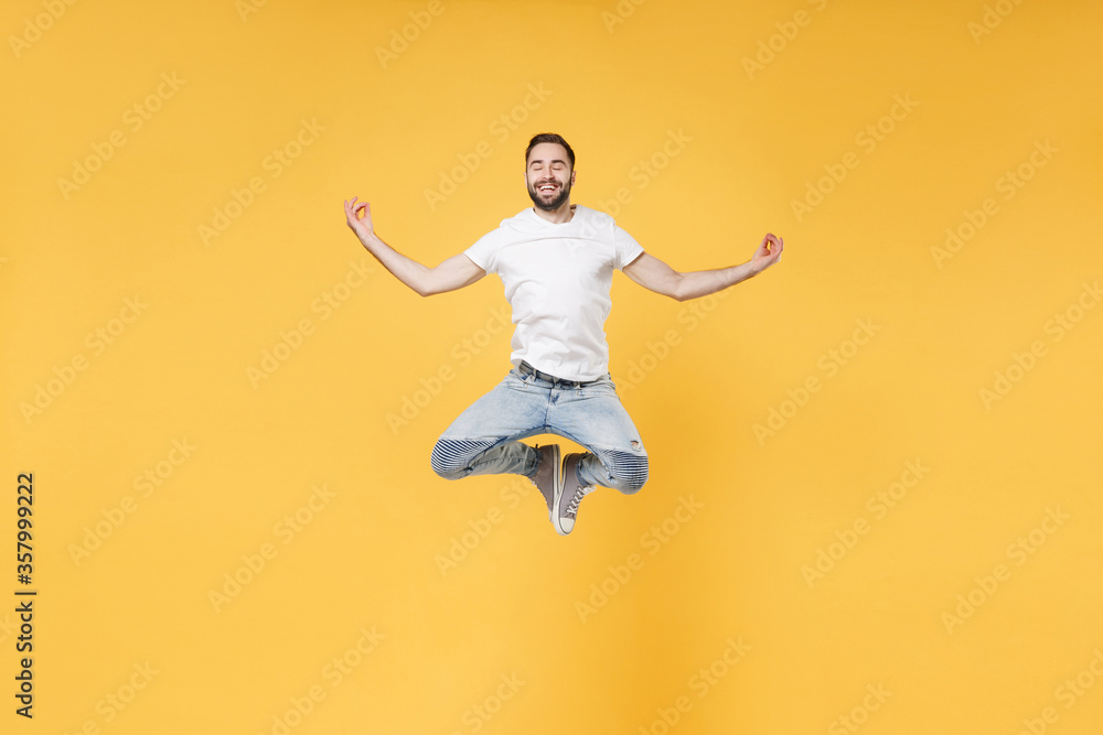 Smiling young bearded man guy in white casual t-shirt posing isolated on yellow background studio. People lifestyle concept. Mock up copy space. Jumping hold hands in yoga gesture relaxing meditating. Smiling young bearded man guy in white casual t-shirt posing isolated on yellow background studio. People lifestyle concept. Mock up copy space. Jumping hold hands in yoga gesture relaxing meditating.