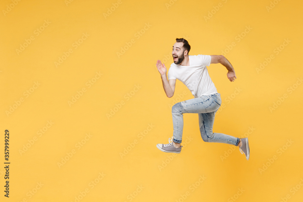 Side view of surprised young bearded man guy in white casual t-shirt posing isolated on yellow wall background studio portrait. People lifestyle concept. Mock up copy space. Jumping like running. Side view of surprised young bearded man guy in white casual t-shirt posing isolated on yellow wall background studio portrait. People lifestyle concept. Mock up copy space. Jumping like running.