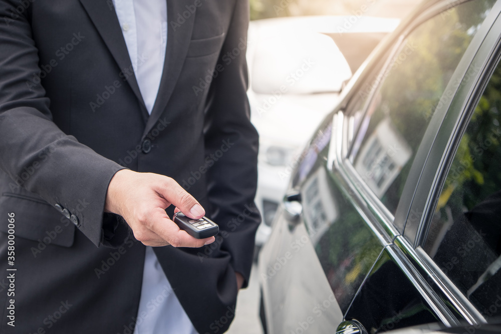 Businessman opens his luxurious car door with a modern remote control key. The young man is locking the automobile with the security system. Keyless in male hand with copy space. Businessman opens his luxurious car door with a modern remote control key. The young man is locking the automobile with the security system. Keyless in male hand with copy space.