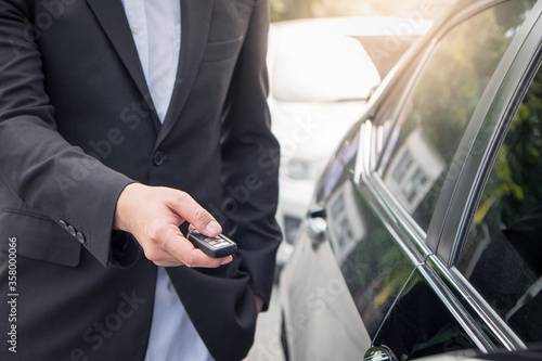 Businessman opens his luxurious car door with a modern remote control key. The young man is locking the automobile with the security system. Keyless in male hand with copy space.