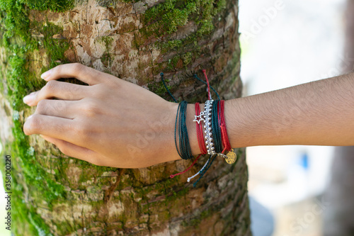 woman's hand with red bracelet touching a tree