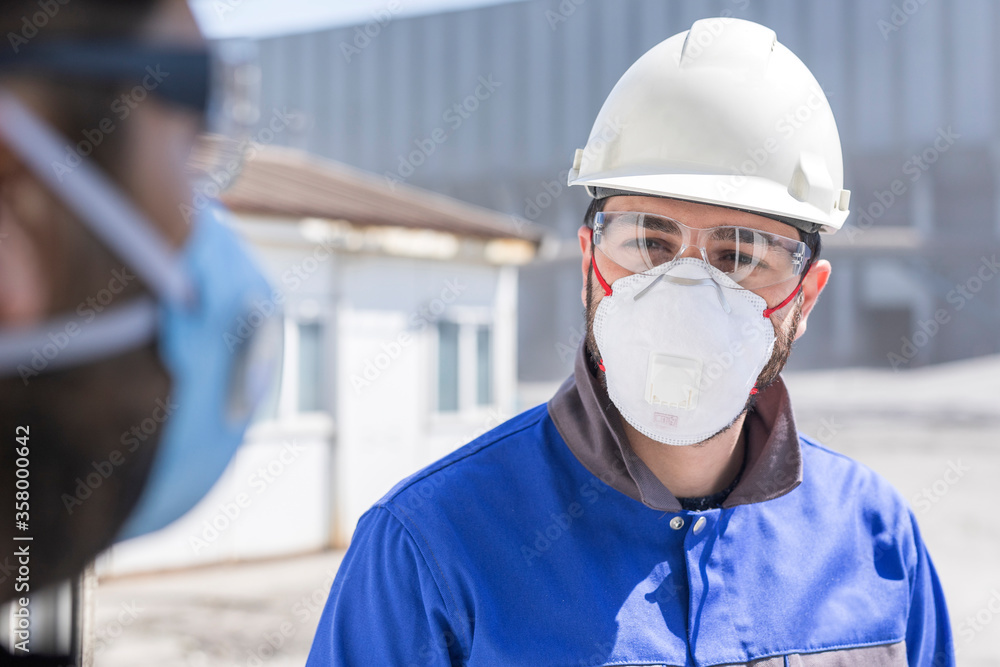 The worker (staff, engineer) protects himself from covid-19 (coronavirus) with a protective mask in the construction site. The worker (staff, engineer) protects himself from covid-19 (coronavirus) with a protective mask in the construction site.