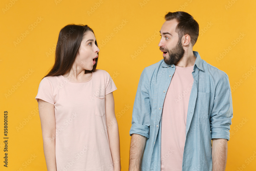 Shocked young couple two friends guy girl in pastel blue casual clothes posing isolated on yellow background. People lifestyle concept. Mock up copy space. Looking at each other, keeping mouth open. Shocked young couple two friends guy girl in pastel blue casual clothes posing isolated on yellow background. People lifestyle concept. Mock up copy space. Looking at each other, keeping mouth open.