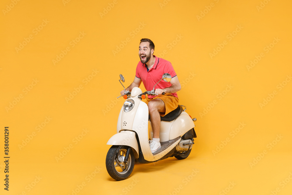 Surprised young bearded man guy in casual summer clothes driving moped isolated on yellow wall background studio portrait. Driving motorbike transportation concept. Mock up copy space. Looking aside. Surprised young bearded man guy in casual summer clothes driving moped isolated on yellow wall background studio portrait. Driving motorbike transportation concept. Mock up copy space. Looking aside.