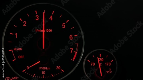 Close up of sports car dashboard with orange luminous dials. PAN to right.