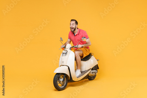 Surprised young bearded man guy in casual summer clothes driving moped isolated on yellow wall background studio portrait. Driving motorbike transportation concept. Mock up copy space. Looking aside. © ViDi Studio