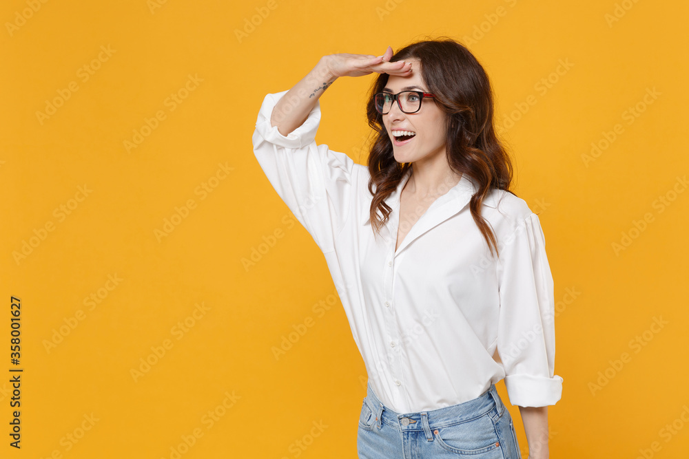 Excited young business woman in white shirt glasses isolated on yellow background. Achievement career wealth business concept. Mock up copy space. Holding hand at forehead looking far away distance. Excited young business woman in white shirt glasses isolated on yellow background. Achievement career wealth business concept. Mock up copy space. Holding hand at forehead looking far away distance.