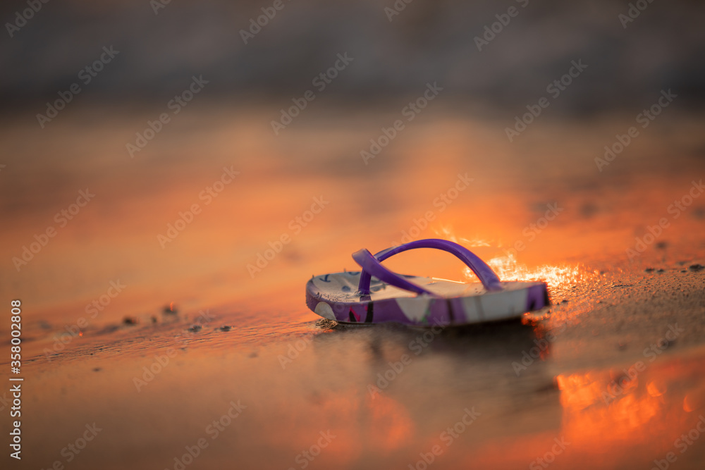 Photo of a washed up flip flop on the beach at sunset Photo of a washed up flip flop on the beach at sunset
