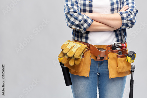 repair, construction and building concept - woman or builder with working tools on belt over grey background © Syda Productions