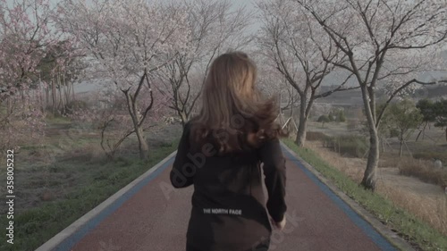 blonde girl running on road under sakura tree