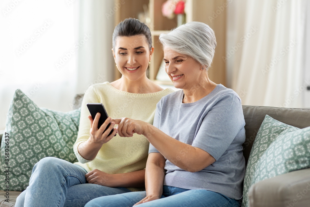 family, generation and technology concept - happy smiling senior mother and adult daughter with smartphone at home