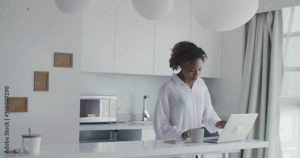 medium shot of a young african lady singing song happily walking towards desk working on computer dancing enjoying music using smartphone then walking away moving body following her humming medium shot of a young african lady singing song happily walking towards desk working on computer dancing enjoying music using smartphone then walking away moving body following her humming