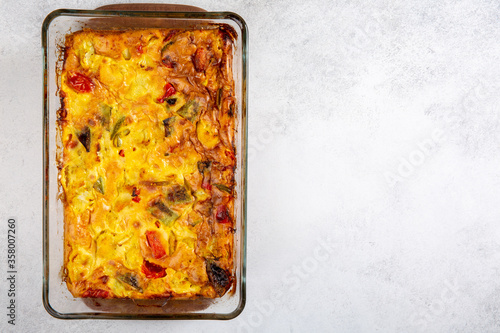 Vegetable clafoutis in glass baking dish on concrete background, savory pie with bell peppers, peas, onions and tomatoes. Top view, copy space.