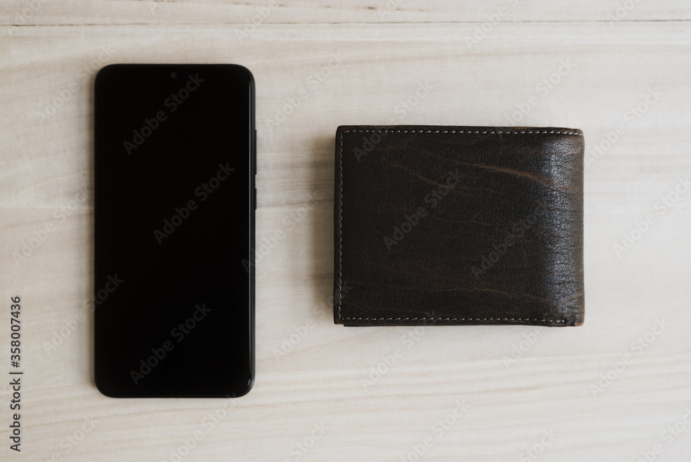 Black mobile phone and brown leather wallet on wooden table, top view. Mobile banking concept. Online wallet Black mobile phone and brown leather wallet on wooden table, top view. Mobile banking concept. Online wallet