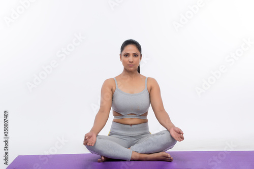 Young woman doing yoga and meditating on exercise mat 