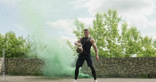 Training with kettlebells, intense strength exercise outdoor with smoke background. Men doing workout with kettlebell