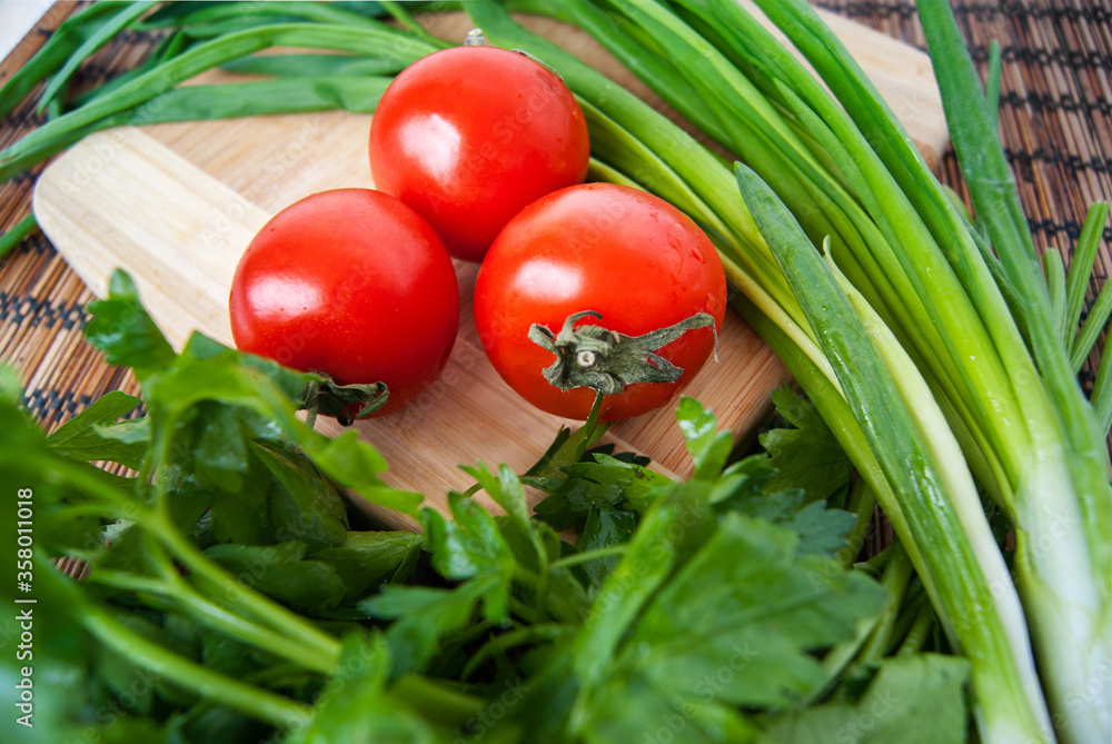 Tomatoes and herbs on a wooden board and a bamboo napkin, top view Tomatoes and herbs on a wooden board and a bamboo napkin, top view