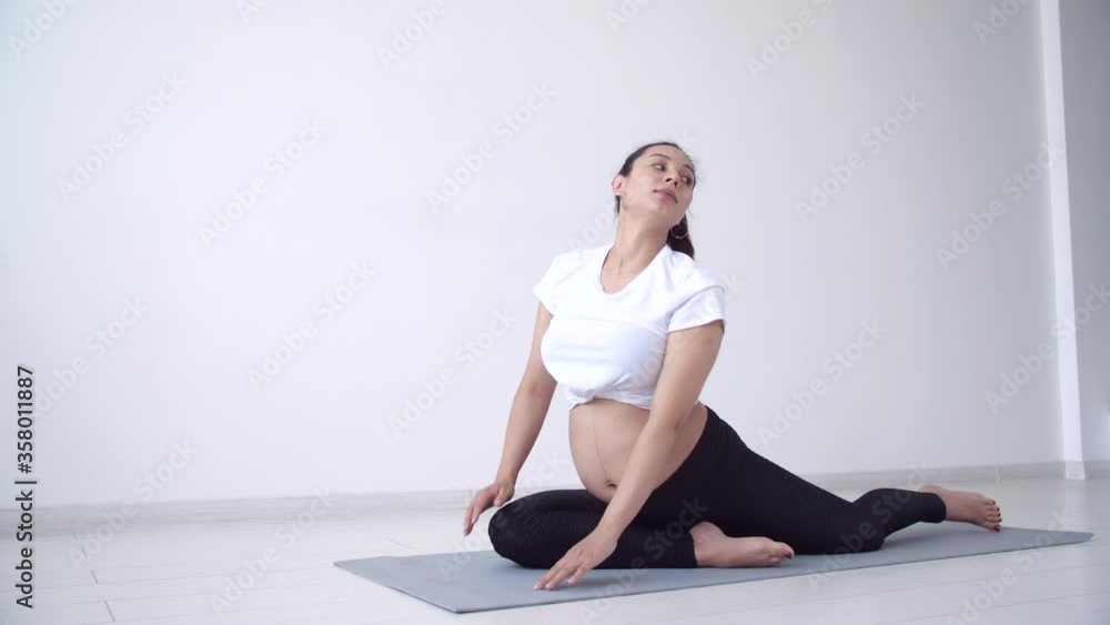 Health concept. Young pregnant woman does yoga exercise in the white room Health concept. Young pregnant woman does yoga exercise in the white room