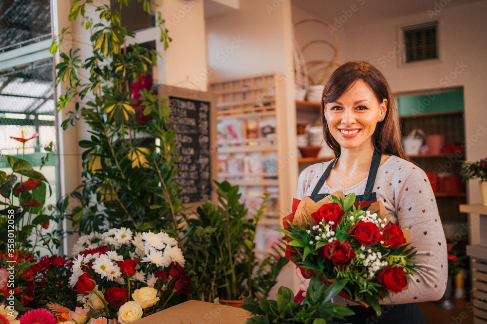 Small business. Portrait of a smiling florist holding bouquet while surrounded with beautiful flowers at floral shop.