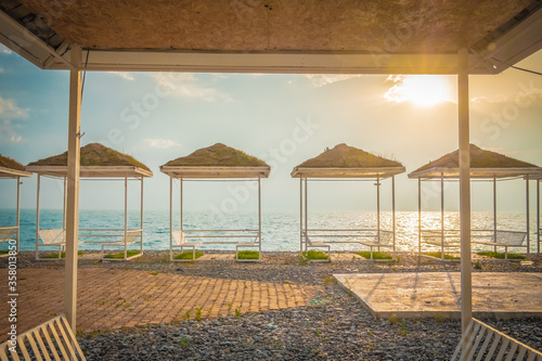 Empty summer cafe on the beach. No visitors due to pandemic and covid-19. Tables on a canopy  wooden flooring. Restaurant with sea view on the coastline. Closed borders  lack of tourists. Evening. Sun