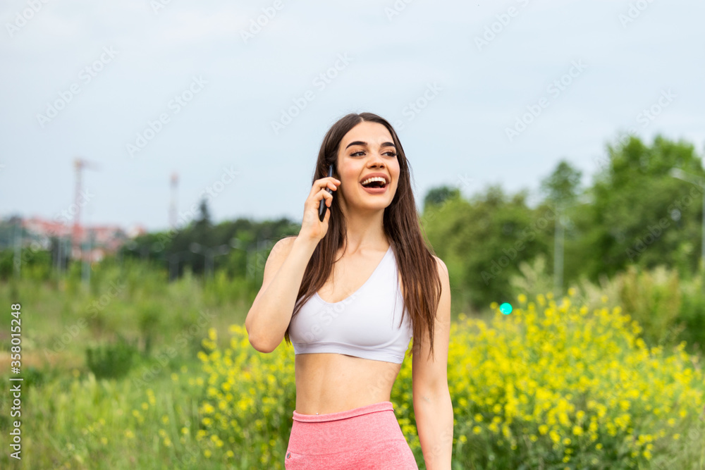 Portrait of a young woman in sportswear talking on phone outdoors while taking break between training, Portrait of a young woman in sportswear talking on phone outdoors while taking break between training,